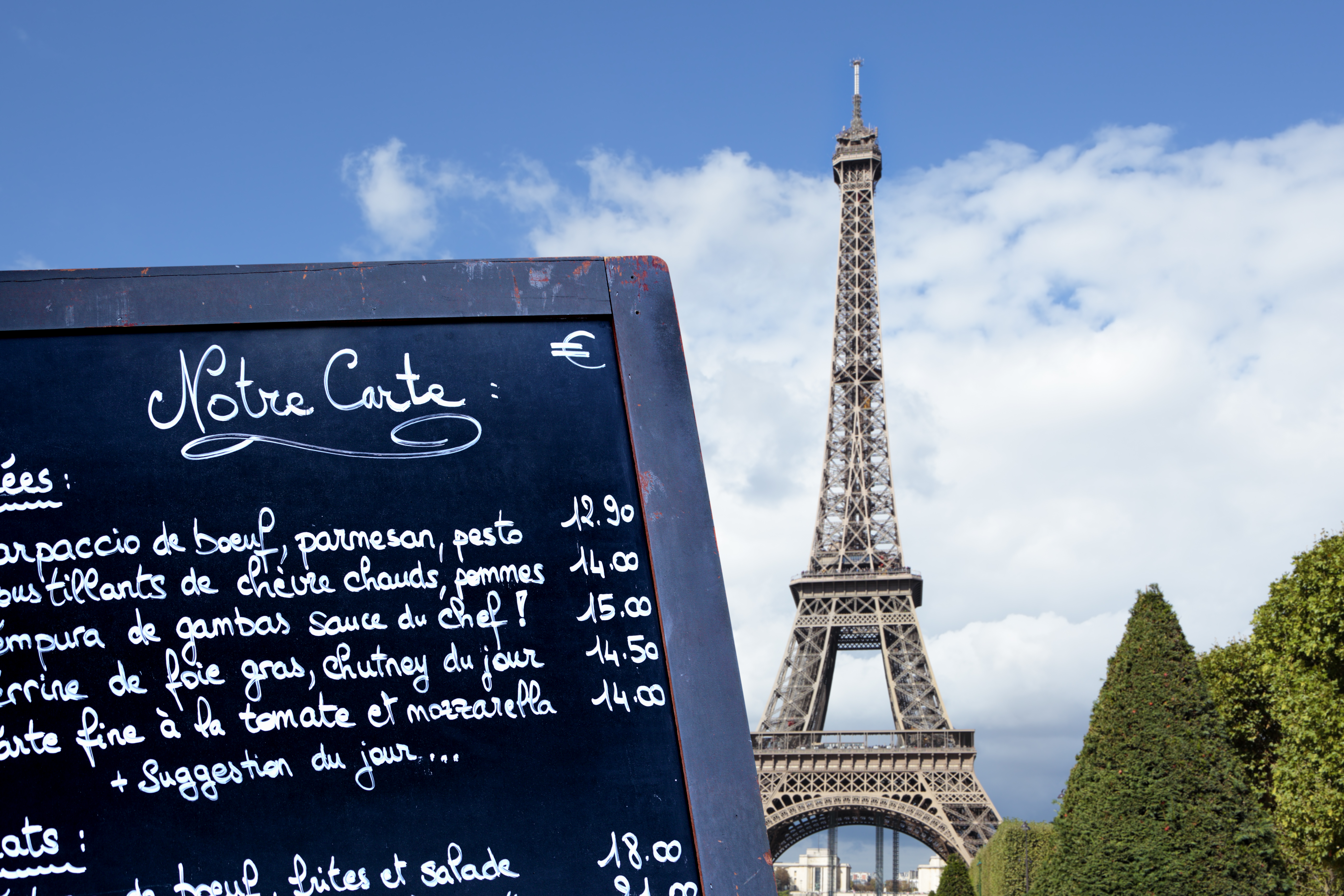 Typical Paris restaurant menu board with Eiffel Tower in the distance.